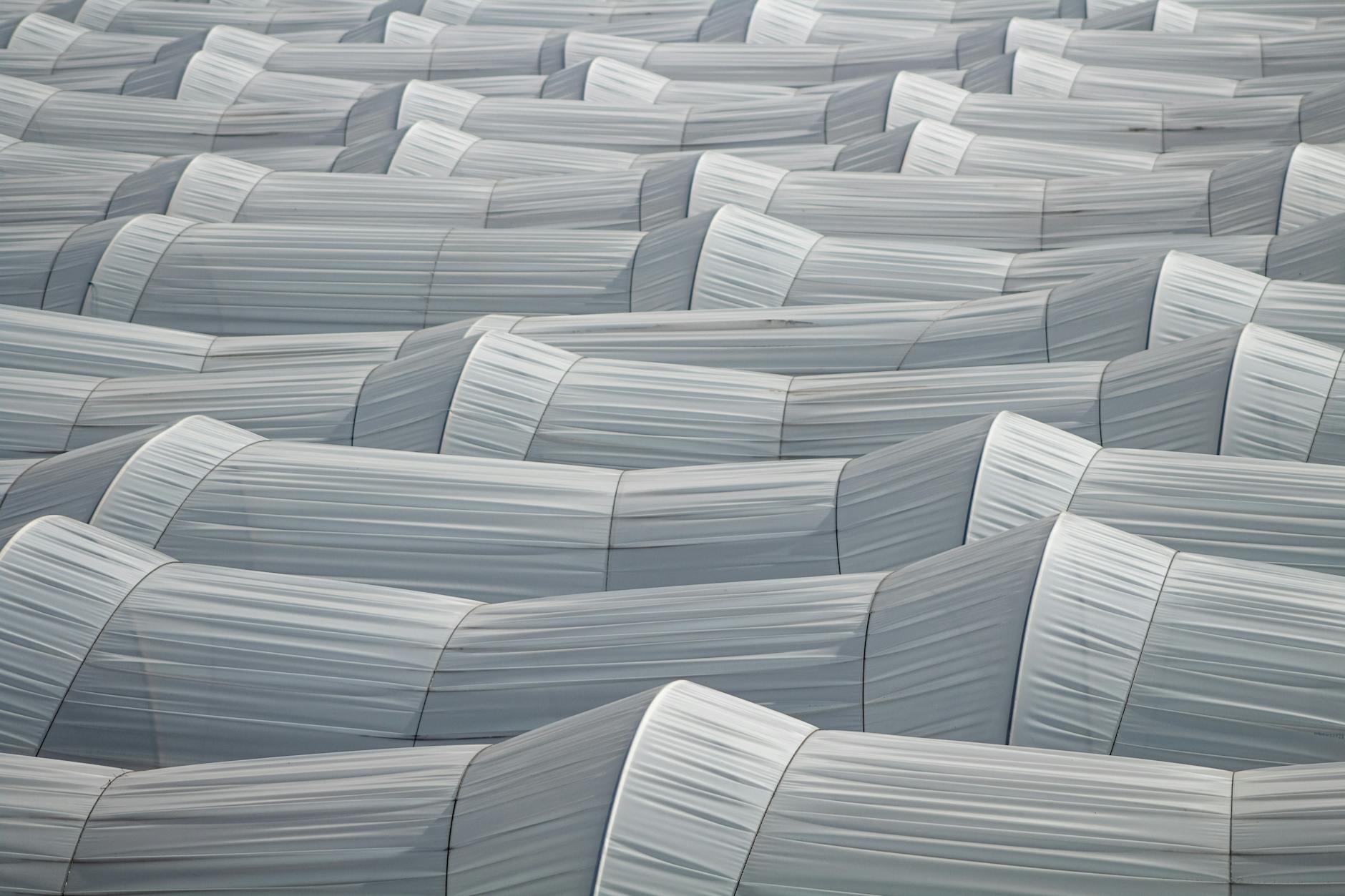 Szeregi tuneli foliowych z góry na tle rolniczego krajobrazu