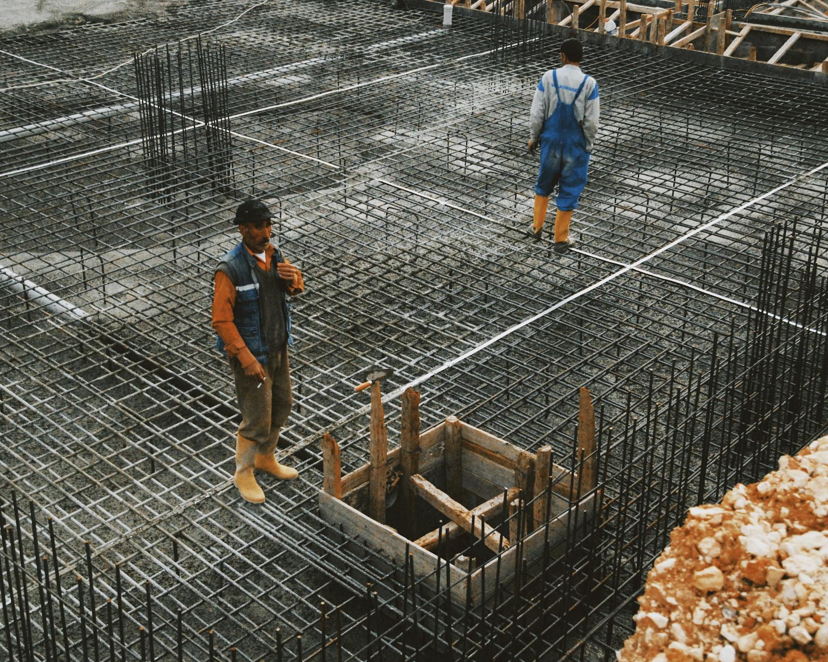 Pracownicy montują stalowe zbrojenie pod betonowy fundament szklarni